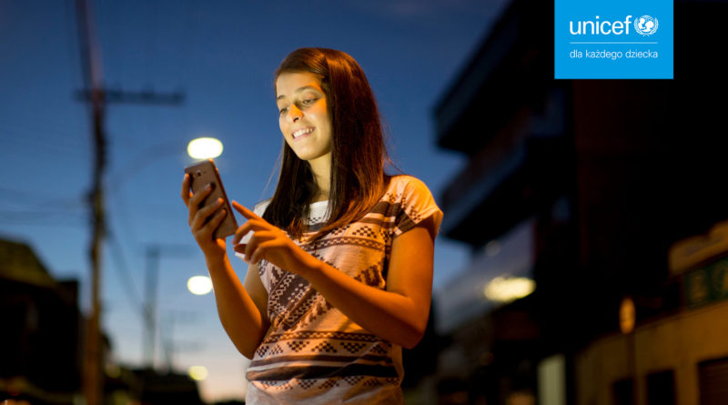Dziewczynka ze smartfonem na tle miejskim, w górnym rogu logo INICEF Polska. Zdjęcie kampanii Przystań w sieci