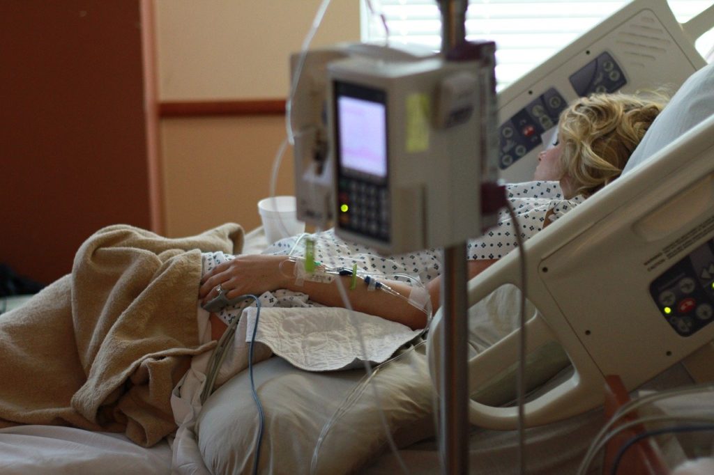 Kobieta w ciąży podczas pobytu w szpitalu, leżąca na łóżku i podłączona do kroplówek i aparatury