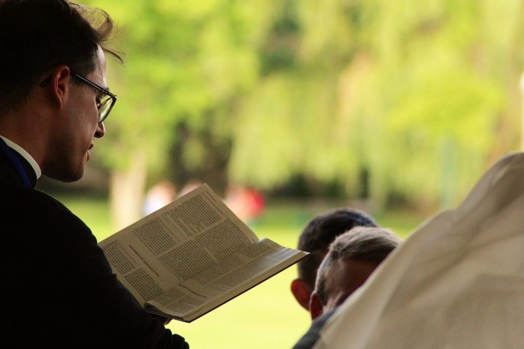 Ksiądz z Biblią modlący się nad głowami kilkuletnich chłopców